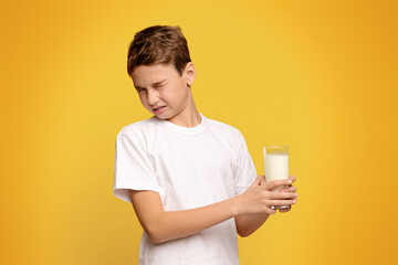 Lactose intolerance. Cute little boy does not want to drink milk, frowning on orange background
