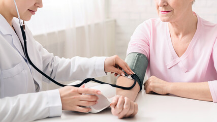 Female doctor measuring blood pressure of senior woman, healthcare concept