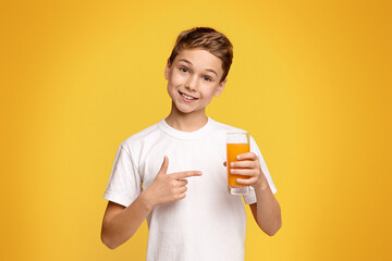 A young boy standing and holding a glass filled with orange juice.