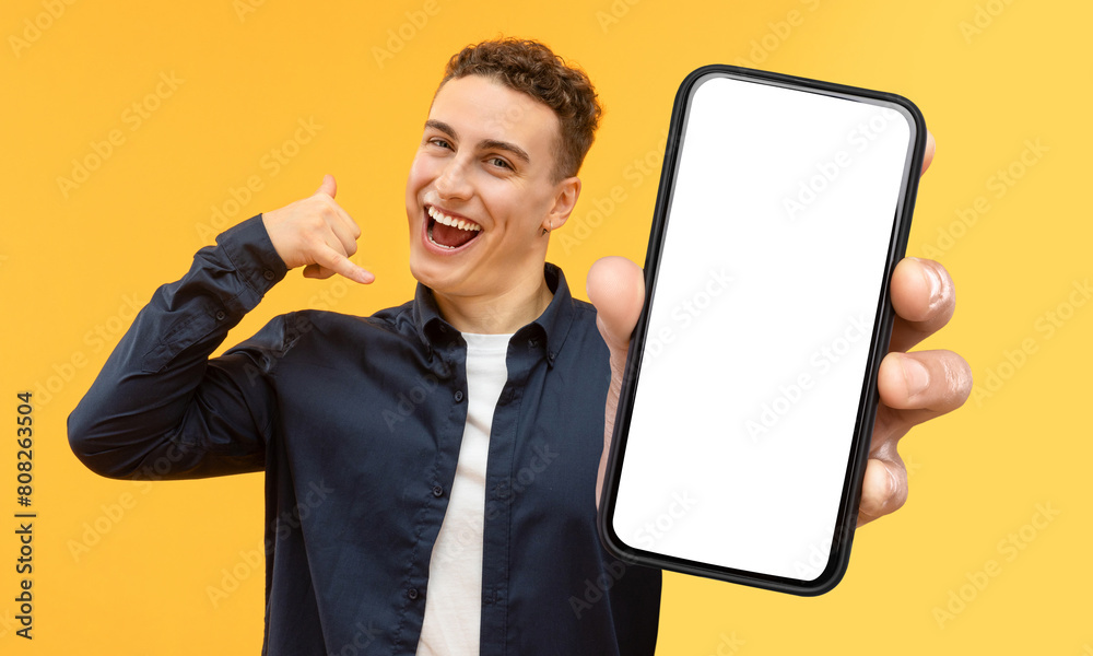 Poster A man stands holding a modern smart phone with white blank screen mockup copy space in his hand, isolated on yellow studio background