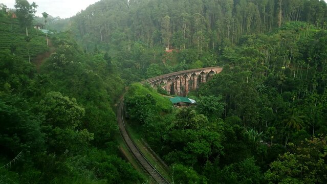 Train crosses Nine Arch Bridge at sunrise in Sri Lanka. Historic railway viaduct with rich jungle backdrop. Iconic transportation captured by drone in warm morning light. Travelers enjoy scenic ride.