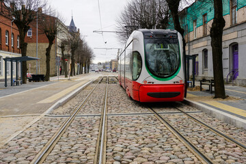 A modern low-floor tram car at a newly built stop platform and paved intermediate track surface - obrazy, fototapety, plakaty