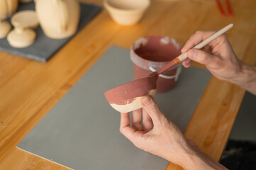 Close-up of a potter's hands with a brush painting ceramic dishes. 