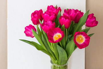 bouquet of bright pink fuchsia tulips in a glass vase on a wooden table	

