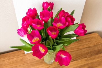 bouquet of bright pink fuchsia tulips in a glass vase on a wooden table	
