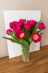 bouquet of bright pink fuchsia tulips in a glass vase on a wooden table	
