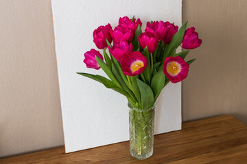 bouquet of bright pink fuchsia tulips in a glass vase on a wooden table	
