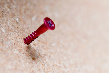 Close up of single red screw on particle board