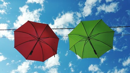 Vibrant red and green umbrellas swaying gently in the breeze against a picturesque blue sky adorned...