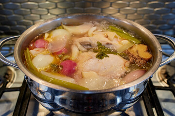 Chicken stock boiling in an oval pot on a gas stove