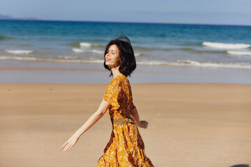 Woman in Yellow Dress Walking with Arms Outstretched on Beach Enjoying Summer Freedom and Happiness