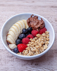 White bowl with red berries, banana, granola and dulce de leche