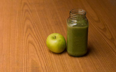 glass of green juice next to green apple on color background