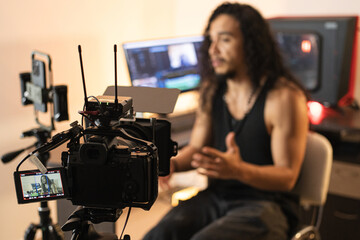 Content Development Workshop. A long-haired content creator immersed in his studio, recording videos with his phone mounted on a tripod. Cameras, lights, and a computer are part of his setup.