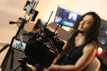 Filming Process in Action. A long-haired content creator immersed in his studio, recording videos with his phone mounted on a tripod. Cameras, lights, and a computer are part of his setup.