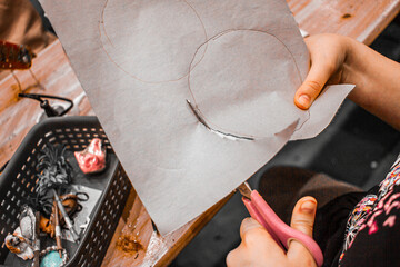 Kids hands with scissors cutting out a circle, miniature items on the table,kids crafting diy