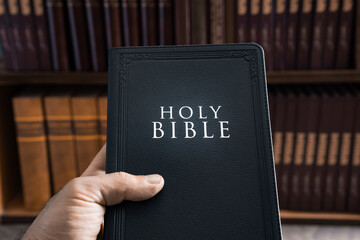 Holy Bible in human hand in library, Christian concept, religious symbol