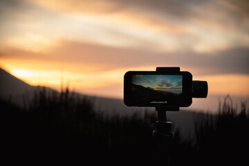 Smartphone on a tripod with active screen shooting sunset in the mountains. Using mobile phone to...