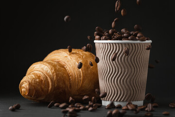 Paper cup full of coffee beans next to freshly baked croissant on the black background. Mock up...