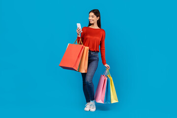 A woman holding shopping bags in one hand and a cell phone in the other. She appears focused on her...