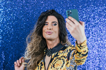 Confident drag queen taking selfies with a mobile phone over a glitter background.