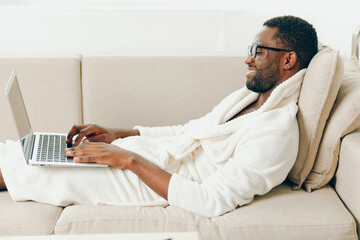 Young African American man working on a laptop in his cozy modern apartment He is sitting on the...