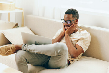 Young African American freelance businessman working on his laptop while sitting on a modern sofa...