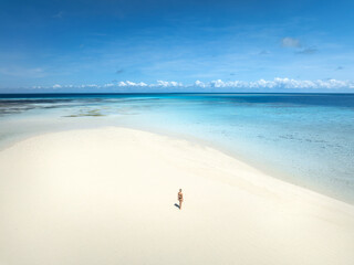 Aerial view of alone young woman on the sandbank in ocean, white sand, blue sea during low tide at...