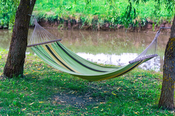 An empty hammock between the trees near the river. Summer camp
