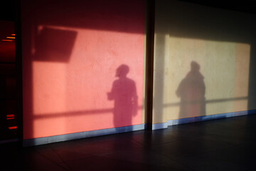 The shadow of a man on the wall, a man watching the departure screen. Silhouettes of people with a reflection on the wall .The shadow of a man on a concrete wall, red in hue. High quality photo