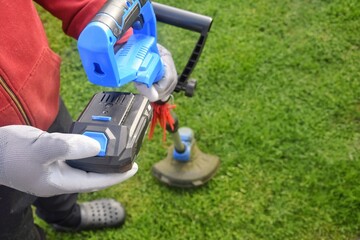 A man installs a battery in a cordless trimmer to mow the grass.