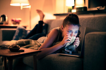 Woman watching a sad movie on laptop at home