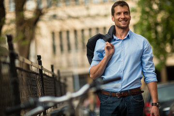 Smiling businessman walking with jacket over shoulder in urban setting