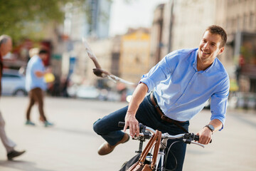 Obraz premium Smiling young businessman riding a bicycle in city