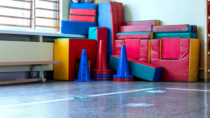 Colorful gym mats and cones stacked in school gymnasium. Educational sports equipment storage