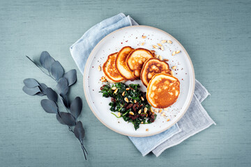 Traditional American pancakes with spinach, pine-nuts and raisins served as top view on a Nordic design plate