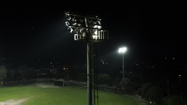 A drone flying towards cricket stadium flood light during a night match.