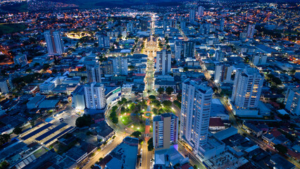 Obraz premium City of Apucarana during the early evening with the yellow lights of Nossa Senhora de Lourdes Cathedral and the bluish sky from the rainy day illuminating the buildings in blue