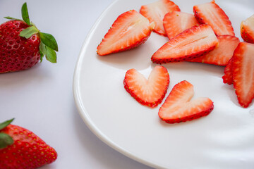 Two pieces of fresh red strawberry cut into a heart shape on a white plate with several more strawberries at the bottom