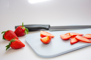 Some fresh red strawberries on a cutting board along with a knife on a white background
