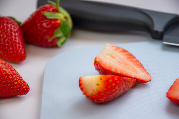 Some fresh red strawberries on a cutting board along with a knife on a white background