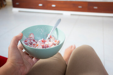 A person holding a turquoise bowl with strawberries cut into small pieces mixed with cream and a...