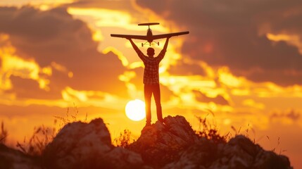 A man stands on the top of a rocky hillside and holds a model airplane above his head as the sun sets behind him.

 - Powered by Adobe