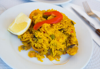 Traditional Valencian paella de mariscos served on white plate with lemon slice