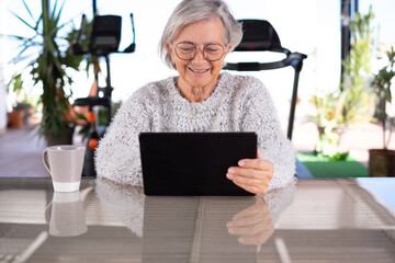 Senior attractive woman using digital tablet sitting outdoor, smiling grey-haired woman looking on...