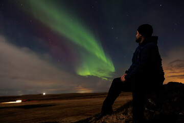 Traveller appreciating northern lights and admiring magical nordic phenomenon, man under icelandic starry night sky looking at aurora borealis. Night photography concept in Iceland.