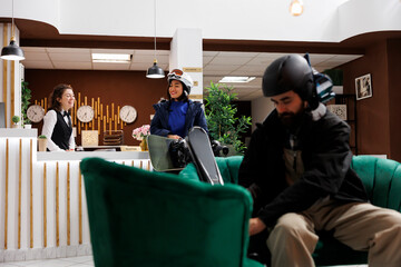 In lounge area friendly concierge assists female tourist with check in at ski resort while young...