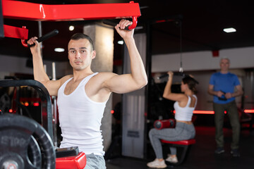 Young athletic man training her arms using machine in gym