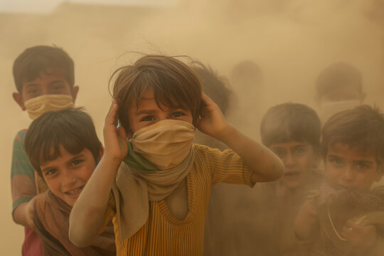 Smiling Child with Scarf Covering Mouth Amidst Dusty Air and Blurred Figures.