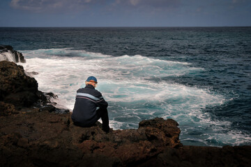 The old man sits on a rock, gazing towards the endless horizon, lost in contemplation